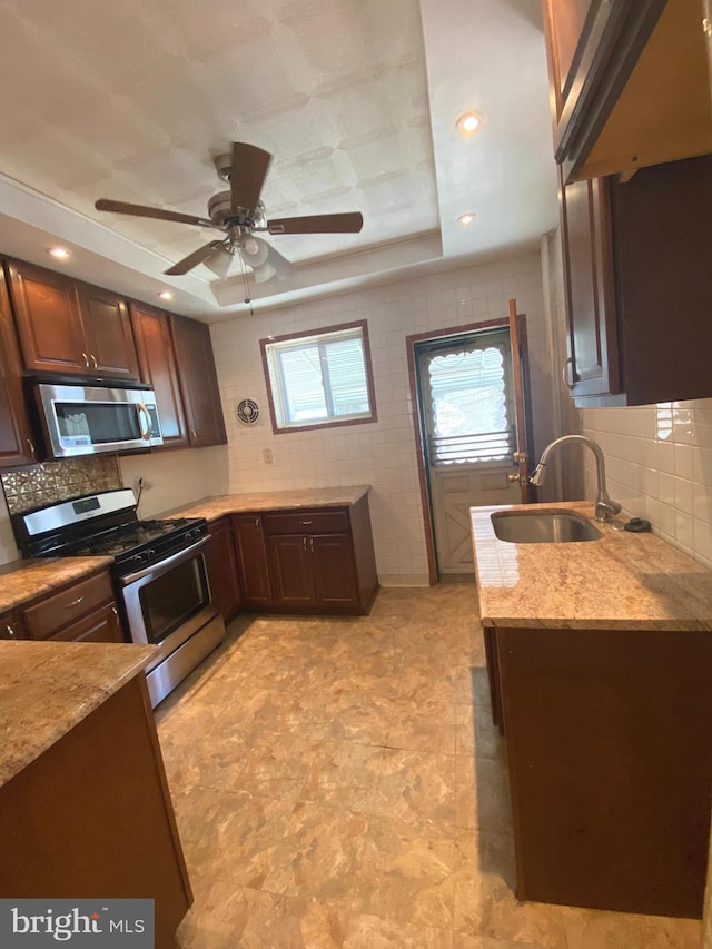 kitchen featuring a tray ceiling, stainless steel appliances, sink, light tile patterned flooring, and ceiling fan