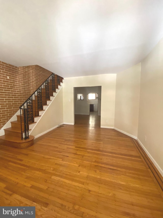 unfurnished living room with hardwood / wood-style flooring and brick wall