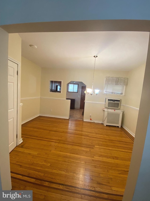 interior space with radiator heating unit, a wall mounted AC, wood-type flooring, and a notable chandelier