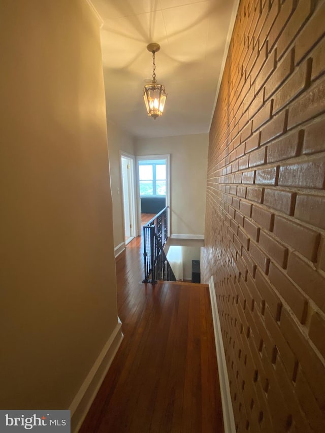 corridor with brick wall, dark hardwood / wood-style flooring, and a notable chandelier