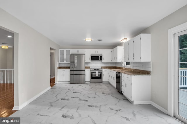 kitchen featuring sink, white cabinetry, dark stone counters, stainless steel appliances, and backsplash