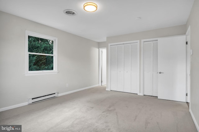 unfurnished bedroom with light carpet, a baseboard heating unit, and two closets