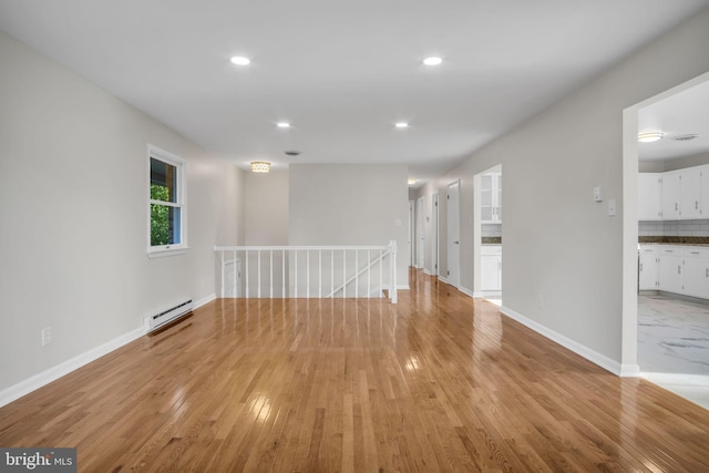 unfurnished room with a baseboard heating unit and light wood-type flooring