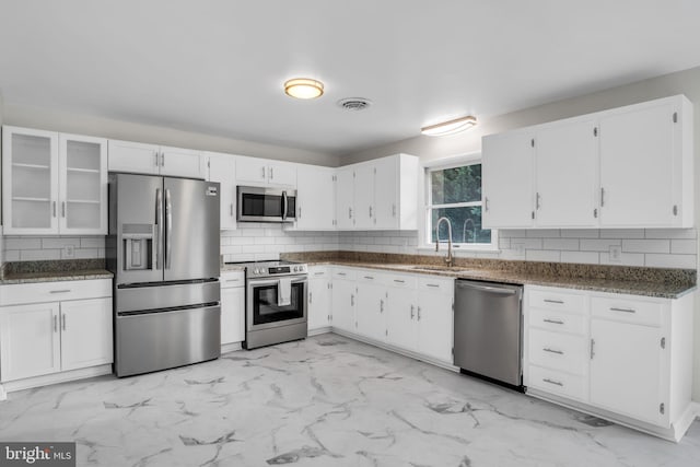 kitchen with appliances with stainless steel finishes, tasteful backsplash, sink, dark stone countertops, and white cabinets