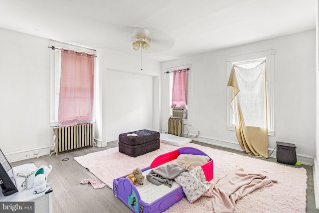 bedroom with ceiling fan, radiator, hardwood / wood-style flooring, and cooling unit