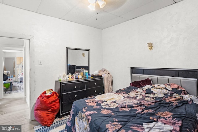 bedroom with ceiling fan, light hardwood / wood-style flooring, and a drop ceiling