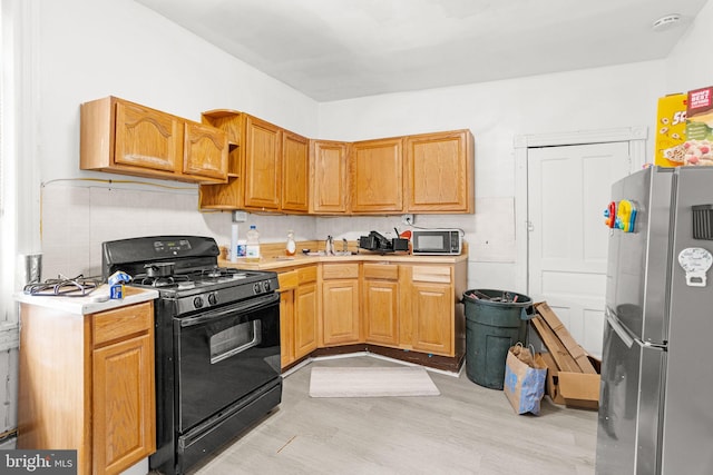 kitchen with backsplash, sink, black appliances, and light hardwood / wood-style floors