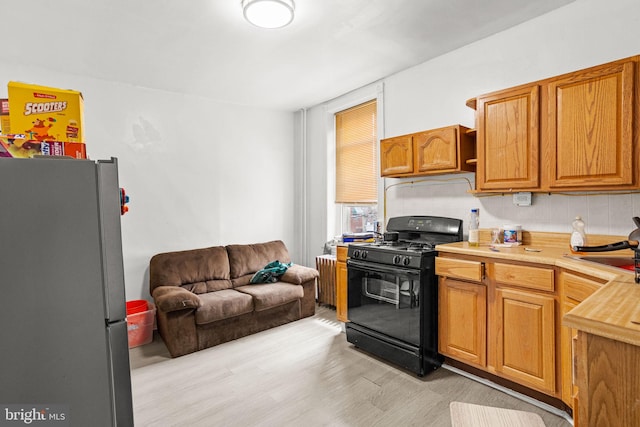 kitchen featuring light wood-type flooring, black gas range oven, and stainless steel refrigerator