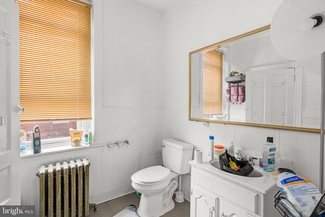 bathroom featuring radiator, toilet, vanity, and tile walls