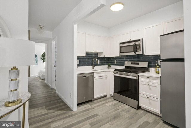 kitchen featuring decorative backsplash, light wood-type flooring, sink, stainless steel appliances, and white cabinetry