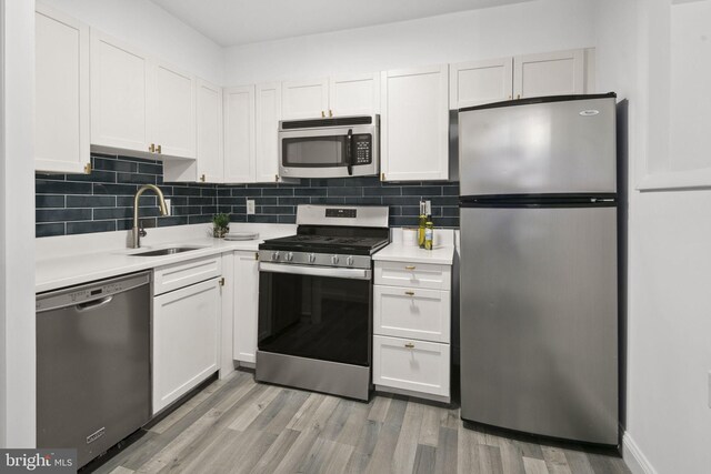 kitchen with stainless steel appliances, white cabinets, sink, and light wood-type flooring