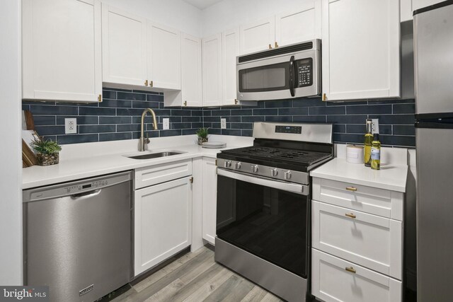 kitchen featuring stainless steel appliances, white cabinets, sink, light hardwood / wood-style flooring, and backsplash