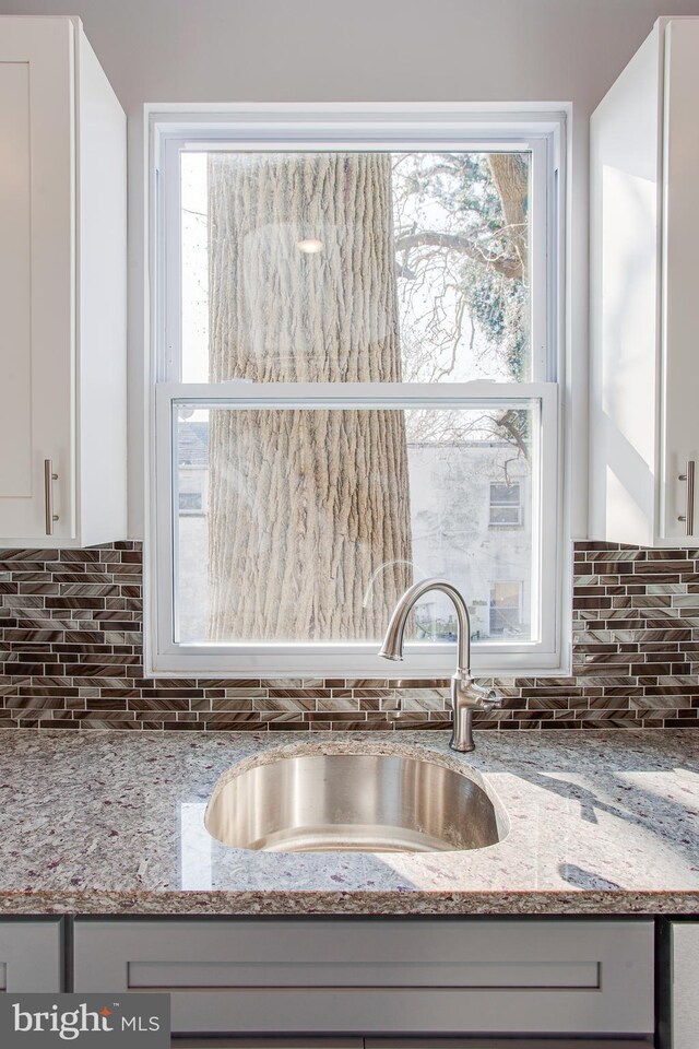 kitchen with white cabinetry, light stone countertops, and sink