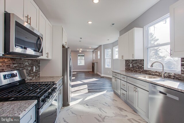 kitchen with tasteful backsplash, light wood-type flooring, light stone counters, appliances with stainless steel finishes, and decorative light fixtures