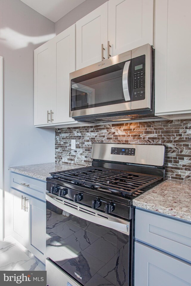 kitchen featuring decorative backsplash, stainless steel appliances, light stone countertops, and white cabinets