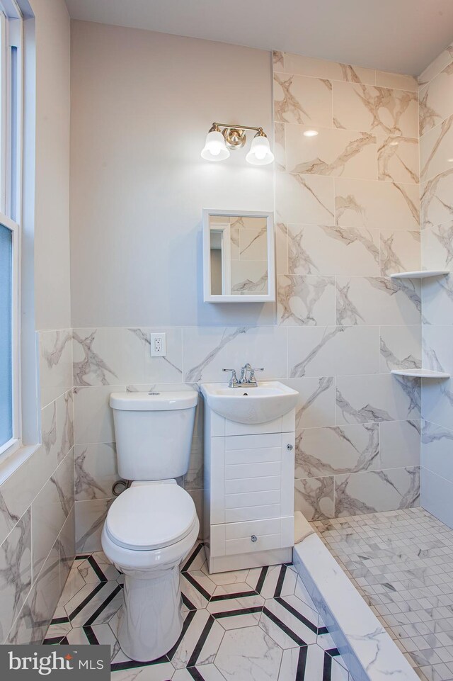 bathroom with a shower, toilet, vanity, tile walls, and tile patterned floors