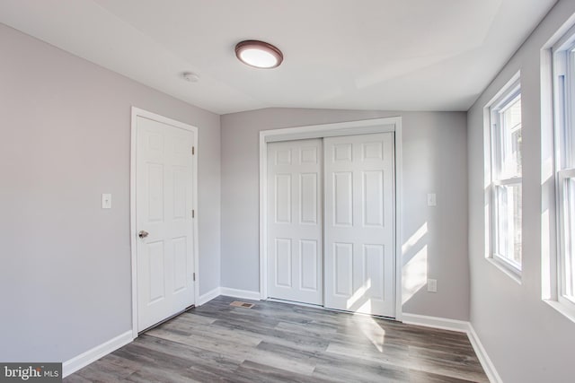 unfurnished bedroom with multiple windows, a closet, wood-type flooring, and vaulted ceiling