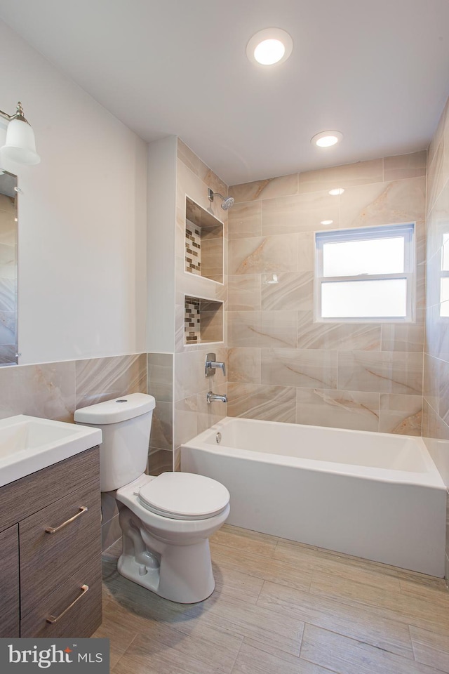 full bathroom with tile patterned flooring, tiled shower / bath, toilet, vanity, and tile walls