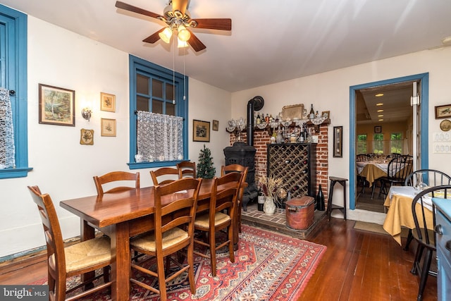 dining space with ceiling fan, a wood stove, and dark hardwood / wood-style floors