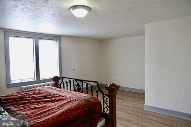 bedroom featuring light hardwood / wood-style floors, radiator, and a textured ceiling