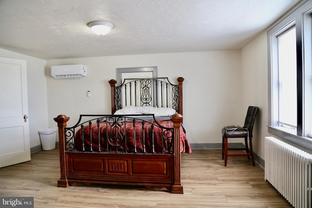 bedroom featuring a wall unit AC, radiator heating unit, and light hardwood / wood-style floors