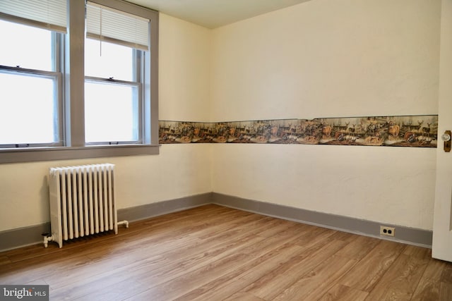 empty room featuring a healthy amount of sunlight, light hardwood / wood-style floors, and radiator heating unit