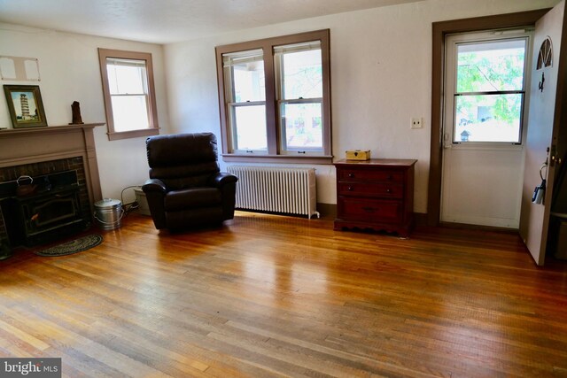 living area with radiator, a brick fireplace, and hardwood / wood-style floors