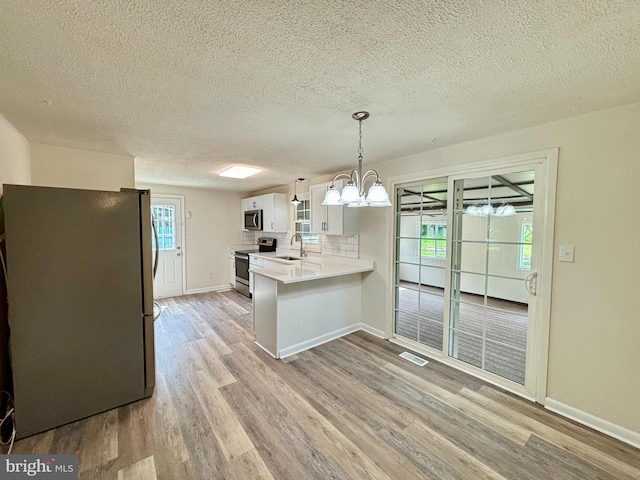 kitchen featuring light wood-type flooring, white cabinets, appliances with stainless steel finishes, sink, and kitchen peninsula