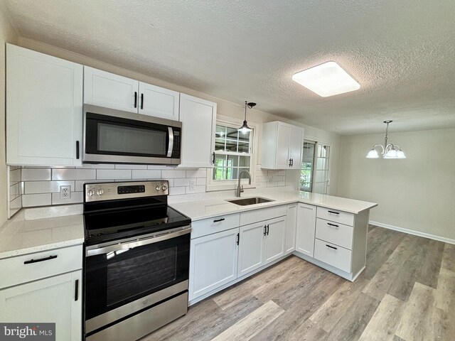 kitchen featuring sink, light wood-type flooring, appliances with stainless steel finishes, a textured ceiling, and kitchen peninsula