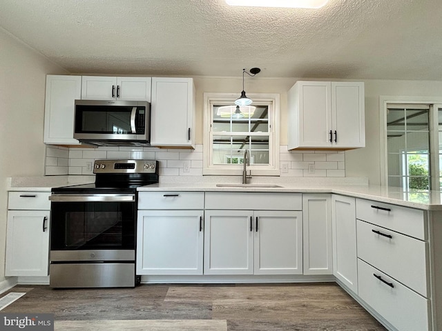 kitchen featuring appliances with stainless steel finishes, decorative light fixtures, light hardwood / wood-style floors, decorative backsplash, and sink