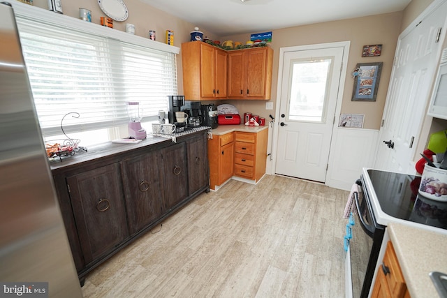 kitchen featuring brown cabinets, light countertops, electric range oven, light wood-style floors, and freestanding refrigerator