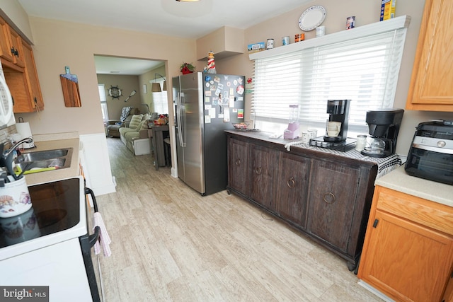 kitchen featuring electric stove, stainless steel fridge with ice dispenser, light countertops, light wood-style floors, and a sink