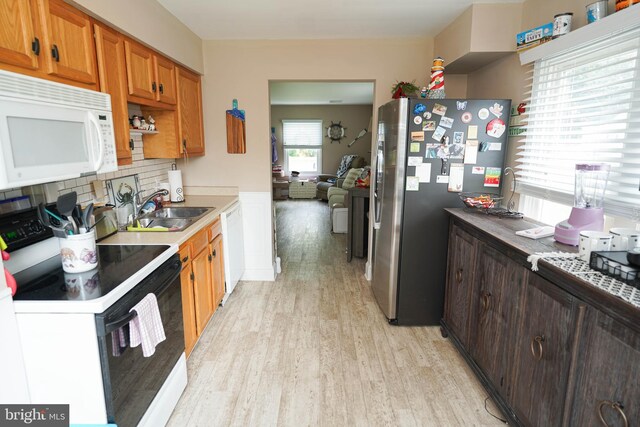 kitchen featuring white appliances, a sink, light wood-style floors, decorative backsplash, and brown cabinets