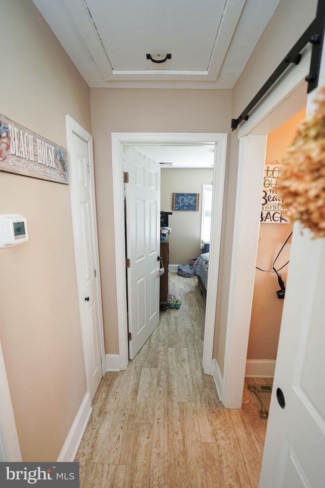 corridor with a barn door, baseboards, light wood-style flooring, and attic access