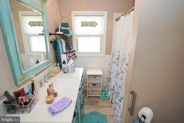 full bath with wainscoting, plenty of natural light, wood finished floors, and vanity