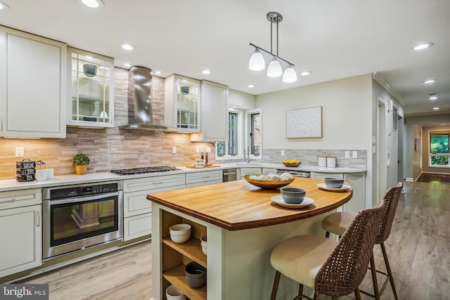 kitchen featuring hanging light fixtures, light hardwood / wood-style flooring, wood counters, stainless steel appliances, and wall chimney exhaust hood