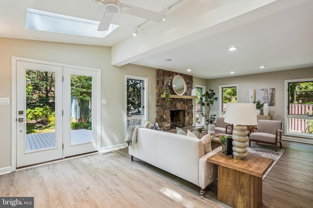 living room with a fireplace, lofted ceiling with skylight, hardwood / wood-style flooring, rail lighting, and ceiling fan