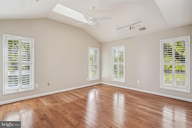 unfurnished room with ceiling fan, vaulted ceiling with skylight, and light hardwood / wood-style floors