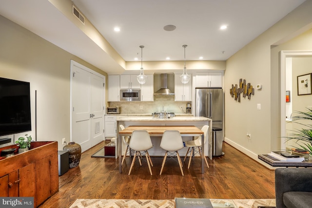 kitchen featuring wall chimney range hood, a breakfast bar area, white cabinetry, stainless steel appliances, and decorative light fixtures