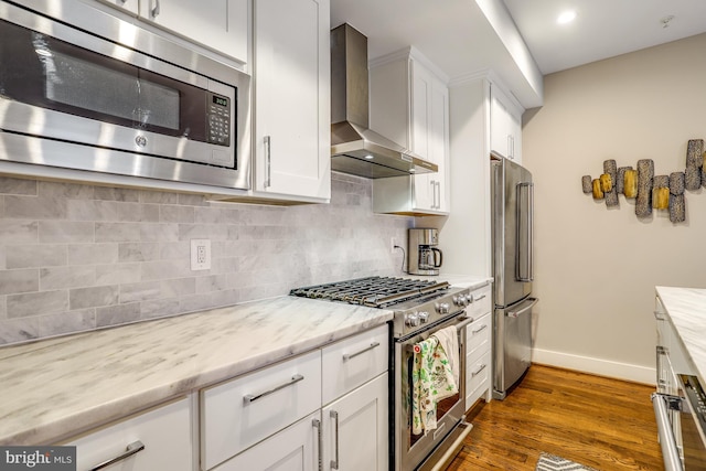 kitchen with white cabinetry, backsplash, light stone counters, premium appliances, and wall chimney exhaust hood