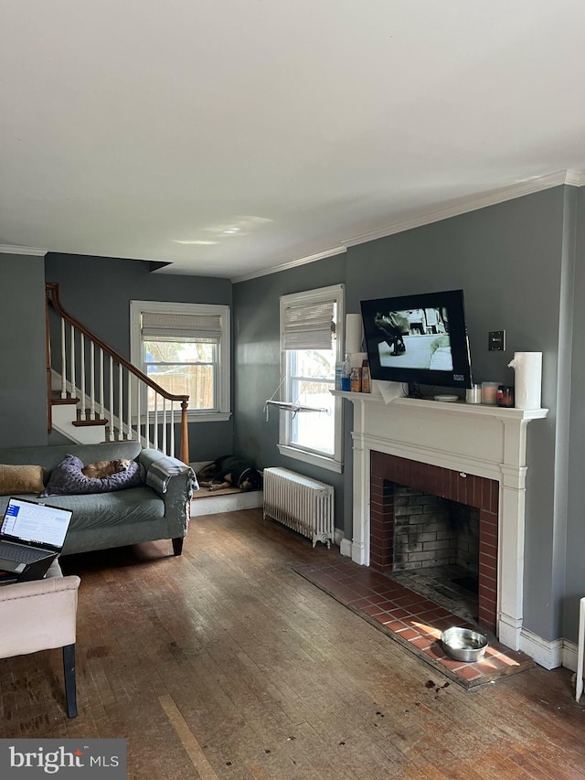 living room featuring ornamental molding, radiator heating unit, hardwood / wood-style floors, and a brick fireplace