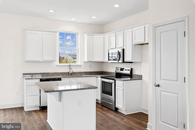 kitchen with sink, appliances with stainless steel finishes, white cabinetry, a kitchen island, and dark stone counters