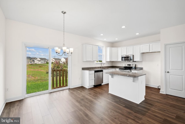 kitchen with decorative light fixtures, a center island, dark stone countertops, stainless steel appliances, and white cabinets