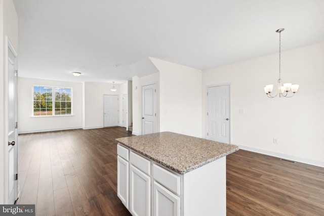 kitchen with dark wood-type flooring, decorative light fixtures, a kitchen island, light stone countertops, and white cabinets