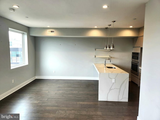 kitchen featuring dark hardwood / wood-style flooring, black double oven, light stone countertops, pendant lighting, and sink