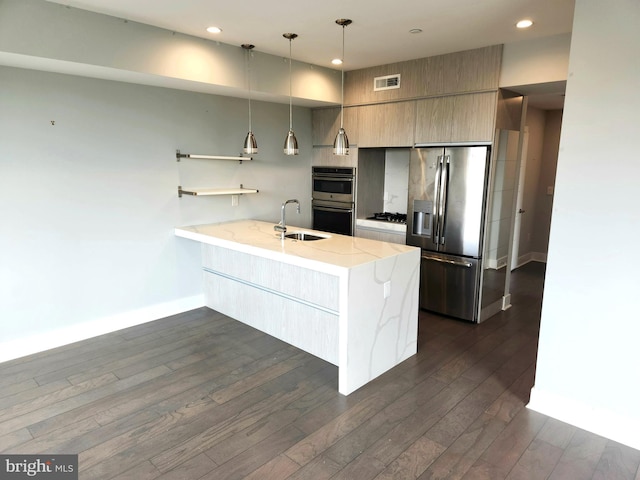 kitchen with appliances with stainless steel finishes, sink, light stone counters, decorative light fixtures, and dark hardwood / wood-style floors