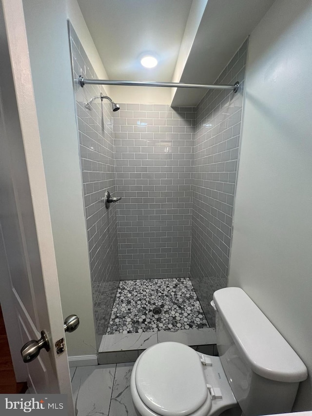 bathroom with tile patterned flooring, toilet, and a tile shower