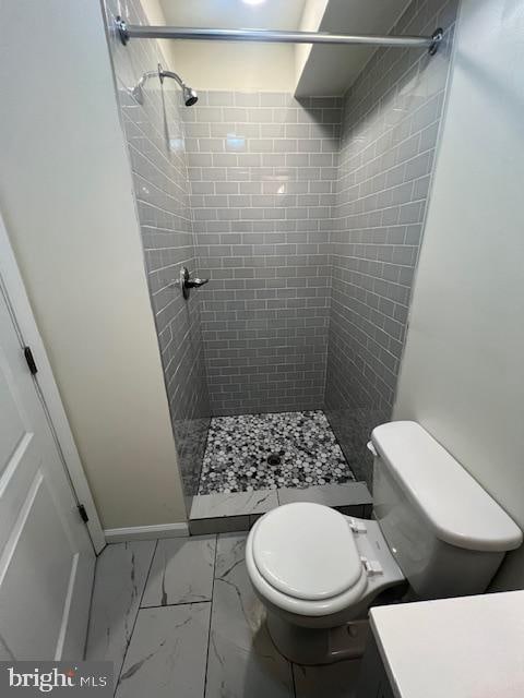 bathroom featuring tile patterned floors, a tile shower, and toilet