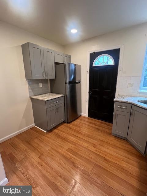 kitchen with light hardwood / wood-style floors, tasteful backsplash, light stone counters, gray cabinetry, and stainless steel fridge