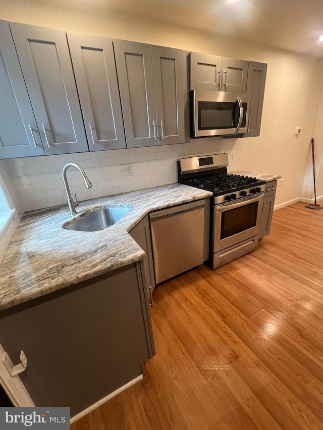 kitchen featuring sink, light hardwood / wood-style flooring, light stone counters, and stainless steel appliances